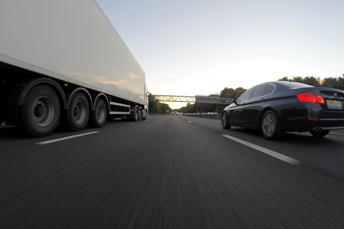 Blue Infiniti Sedan Running on Road Togerther With White Freight Truck